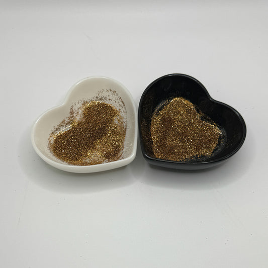 Two heart shaped containers, one black, one white, containing a gold extra fine glitter mix.