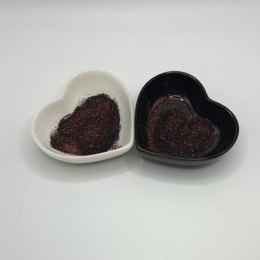 Two heart shaped containers, one black, one white, containing a dark brown extra fine glitter mix.