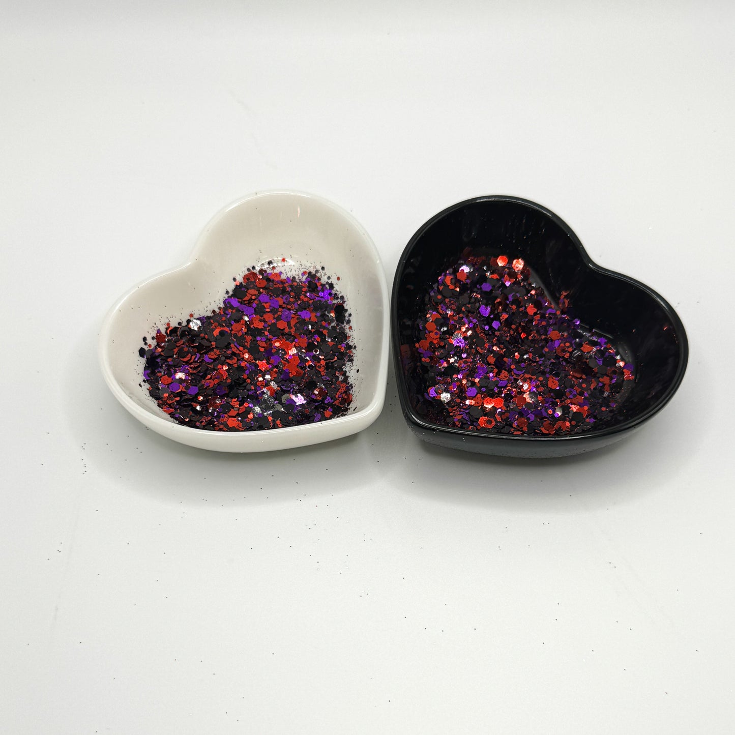 Two heart shaped containers, one black, one white, containing a Black/Red/Purple chunky glitter mix.