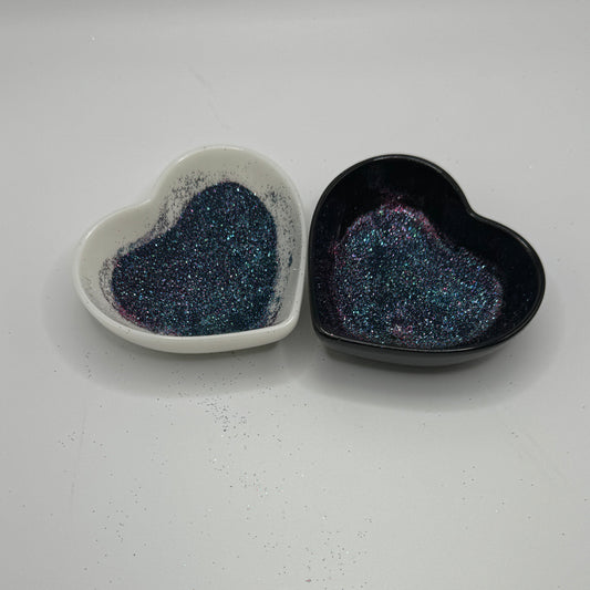 Two heart shaped containers, one black, one white, containing a dark extra fine glitter mix.