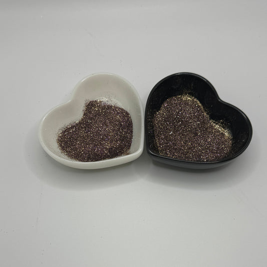 Two heart-shaped dishes, one white and one black, containing multi coloured glitter.