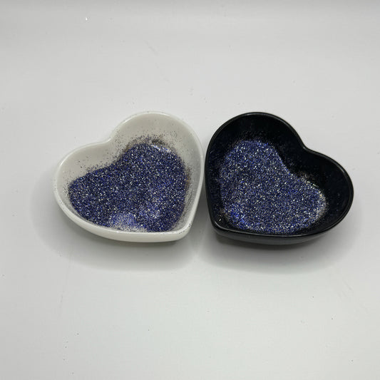 Two heart shaped containers, one black, one white, containing a blue/silver extra fine glitter mix.
