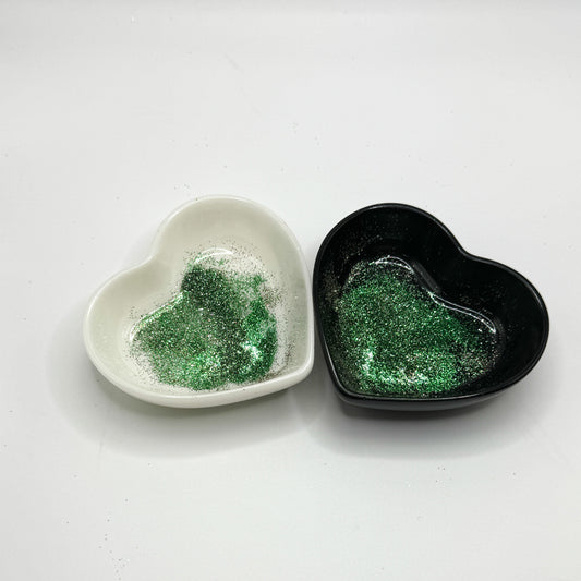 Two heart-shaped dishes, one white and one black, both containing green polyester glitter.