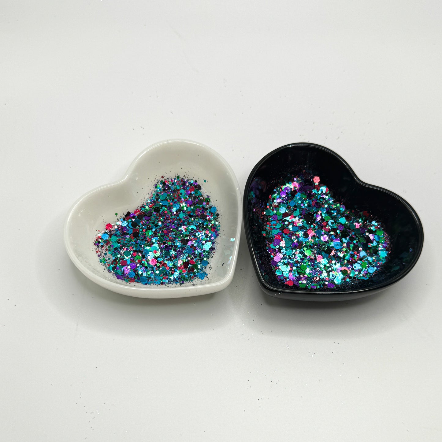 Two heart shaped containers, one black, one white, containing a Green/Black/Purple/Pink/Teal/Blue chunky glitter mix.