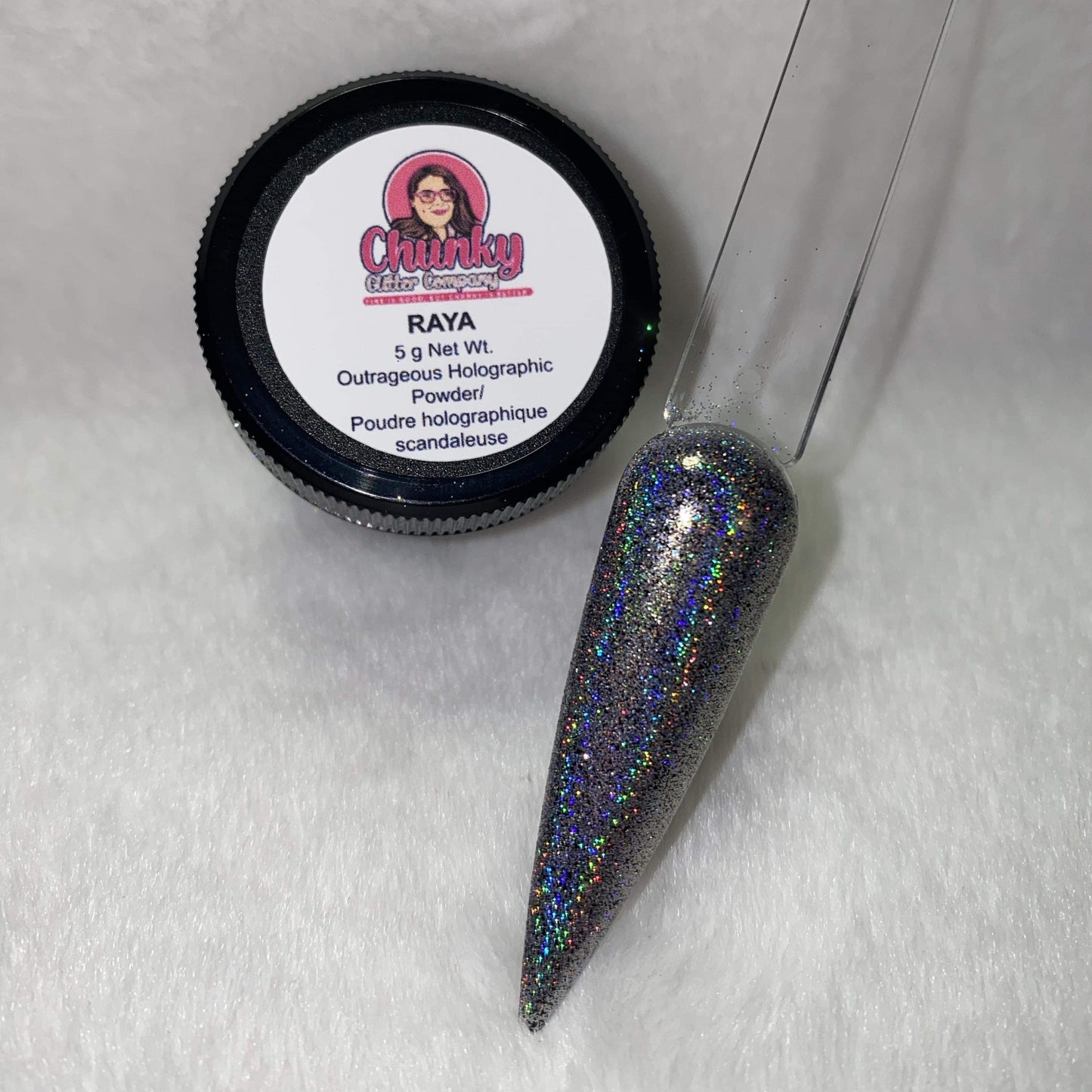A small jar of silver holographic glitter powder next to a sample application on a clear nail.