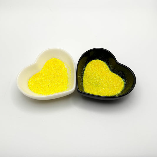 Two heart-shaped dishes, one white and one black, both containing yellow colored glitter.