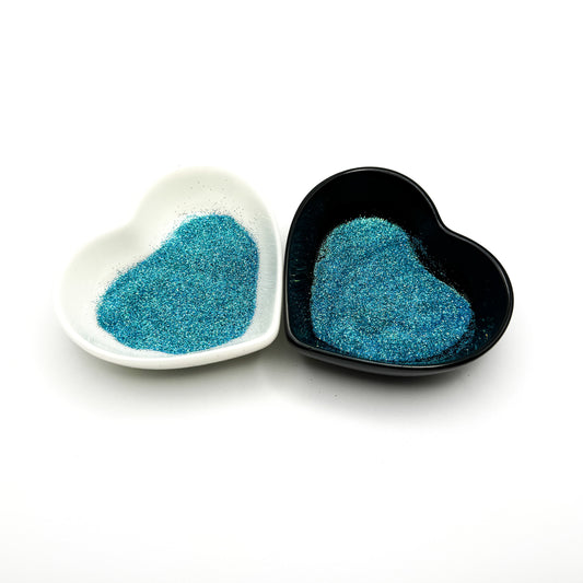 Two heart-shaped dishes, one white and one black, filled with blue colored glitter.