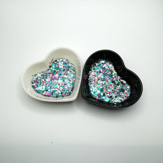 Two heart shaped containers, one black, one white, containing a Teal/Purple/Silver/Gunmetal chunky glitter mix with hexagons and stars.