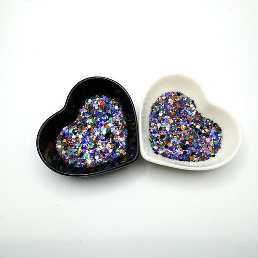 Two heart shaped containers, one black, one white, containing a Hunter Green/Indigo/Bronze/Gold chunky glitter mix.
