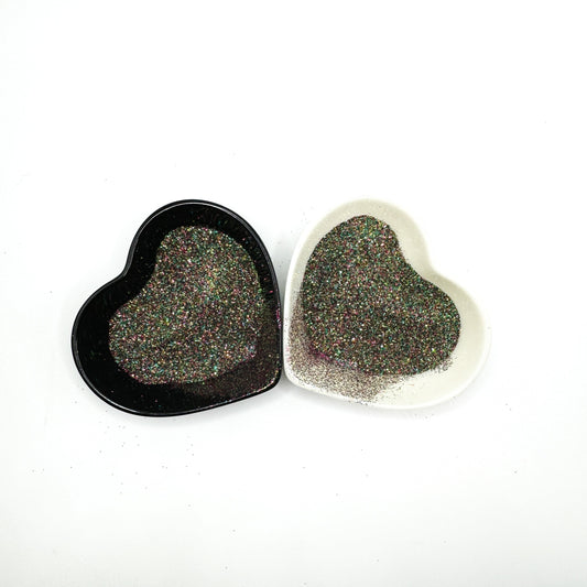 Two heart-shaped containers of glitter, one black and the other white, both showing an extra fine, multicoloured glitter mix