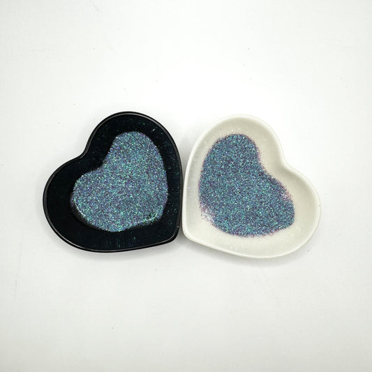 Two heart-shaped containers of glitter, one black and the other white, both showing an extra fine, blue, purple multicoloured glitter mix