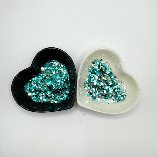 Two heart shaped containers, one black, one white, containing a Teal/Gold/Silver chunky glitter mix.