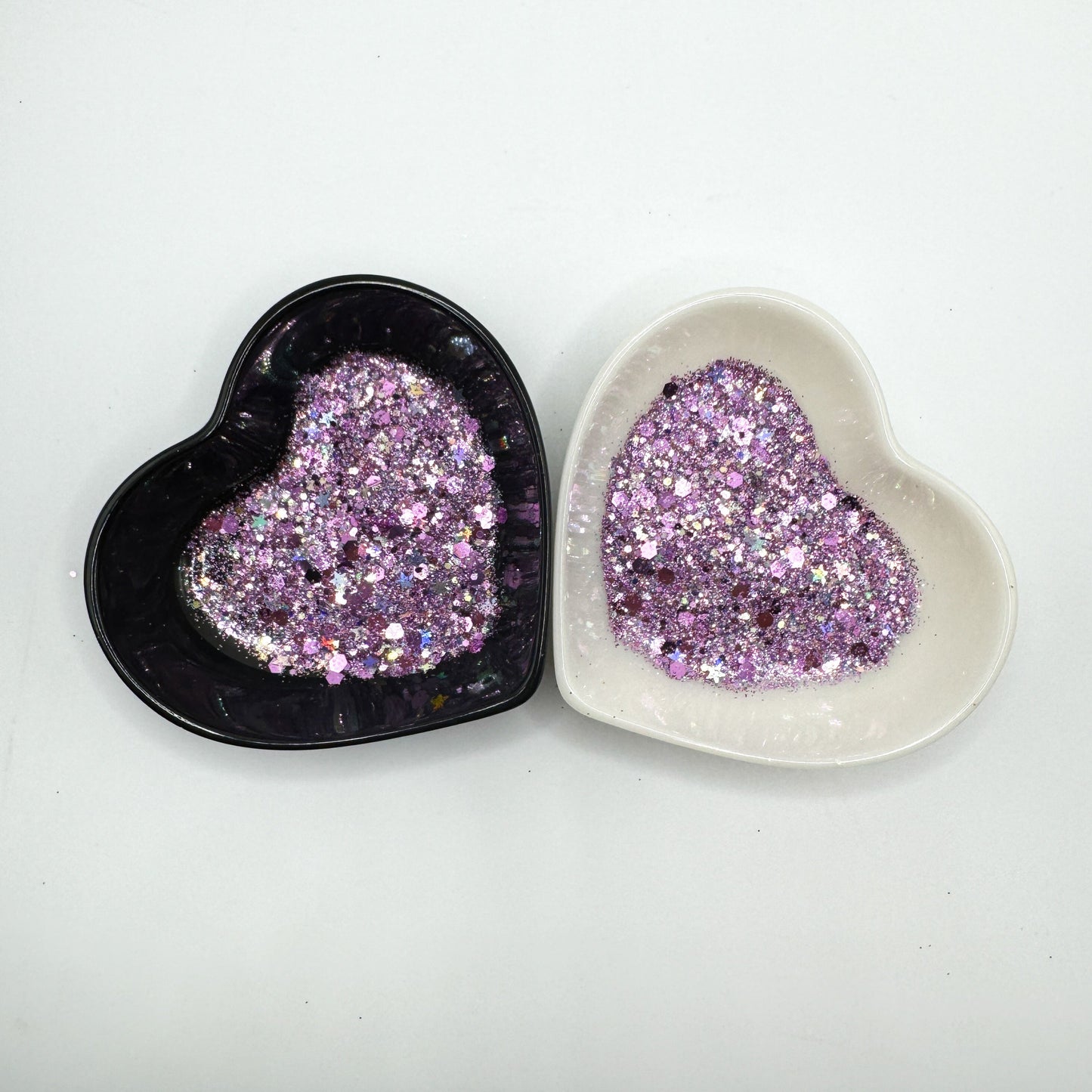 Two heart shaped containers, one black, one white, containing a Purple/Silver chunky glitter mix with hexagons and stars.