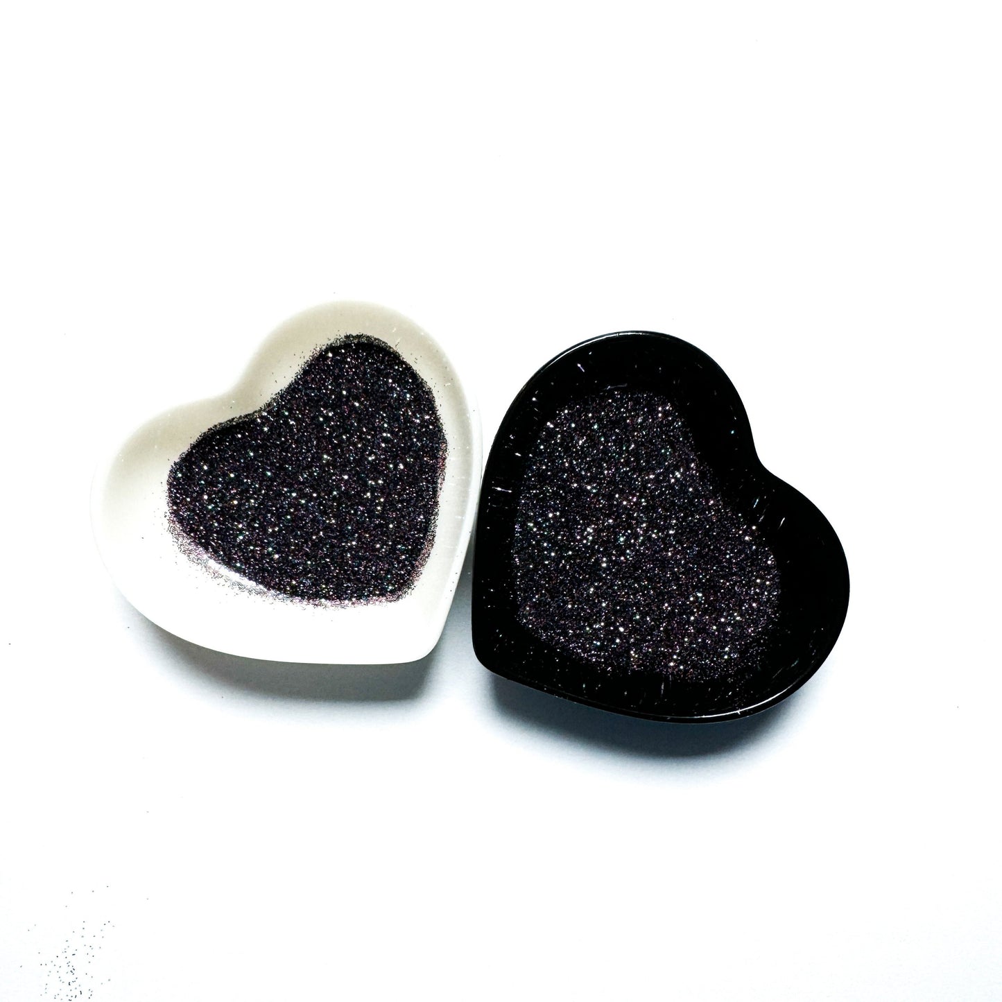 Two heart-shaped containers of glitter, one black and the other white, both showing an extra fine, multicolored glitter mix.