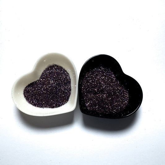 Two heart-shaped containers of glitter, one black and the other white, both showing an extra fine, multicolored glitter mix.