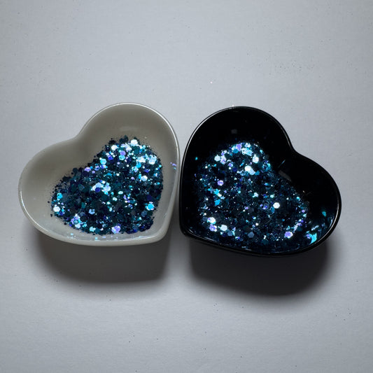 Two heart shaped containers, one black, one white, containing a Blue/Indigo chunky glitter mix.