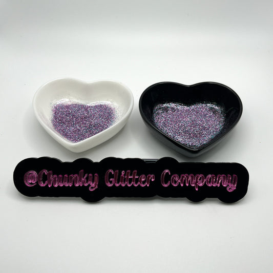 Two heart shaped containers, one black, one white, containing a multicoloured extra fine glitter mix, with a label in front that reads '@ChunkyGlitterCompany'.