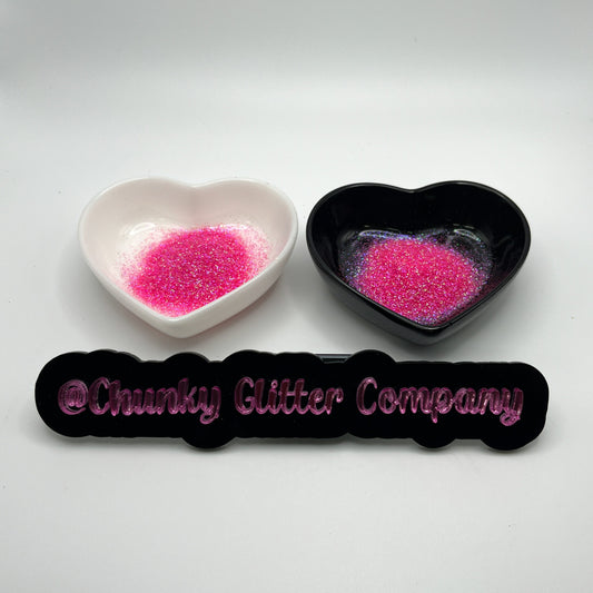 Two heart shaped containers, one black, one white, containing a Pink extra fine glitter mix, with a label in front that reads '@ChunkyGlitterCompany'.