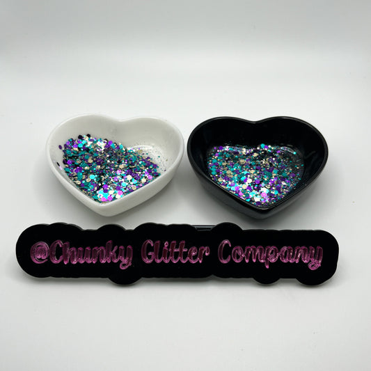 Two heart shaped containers, one black, one white, containing a Light Teal/Purple/Gold chunky glitter mix, with a label in front that reads '@ChunkyGlitterCompany'.