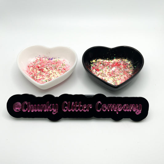 Two heart shaped containers, one black, one white, containing a Light Pink/Green chunky glitter mix, with a label in front that reads '@ChunkyGlitterCompany'.