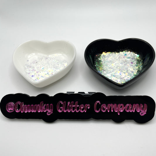 Two heart shaped containers, one black, one white, containing a White/Rainbow/Silver chunky glitter mix, with a label in front that reads '@ChunkyGlitterCompany'.