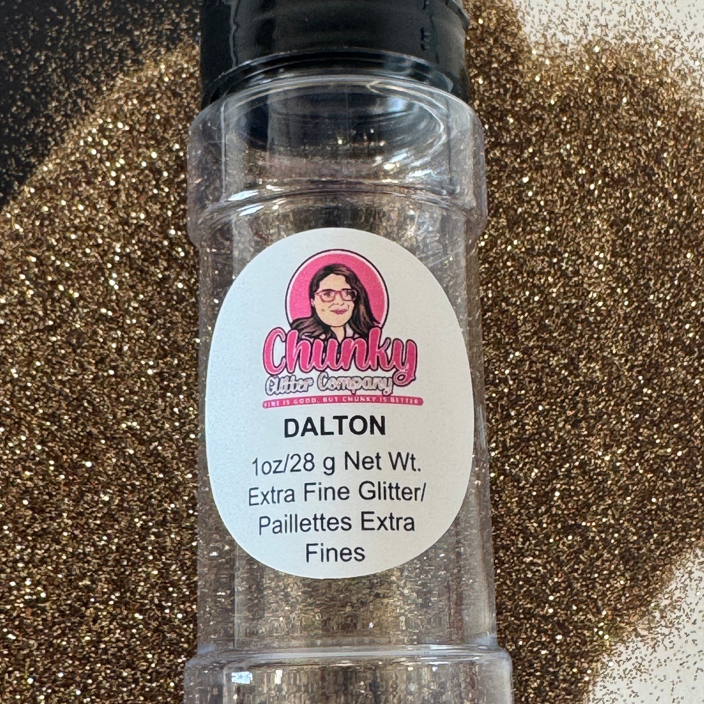 A clear plastic shaker bottle labeled 'Dalton' containing extra fine gold glitter, with a pile of glitter scattered in the background.