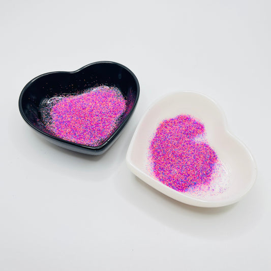 Two heart-shaped dishes, one black and one white, containing pink and blue matte glitter.