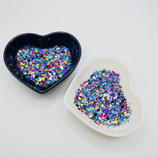 Two heart shaped containers, one black, one white, containing a Black/Rainbow chunky glitter mix.