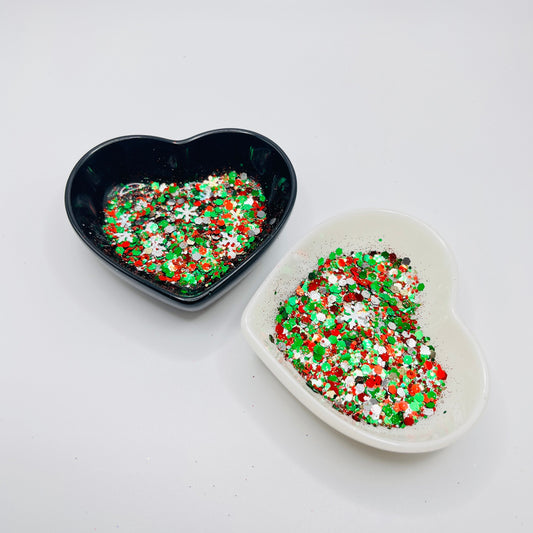 Two heart shaped containers, one black, one white, containing a Red/Green/White/Silver/Gold chunky glitter mix with hexagons and Snowflakes.