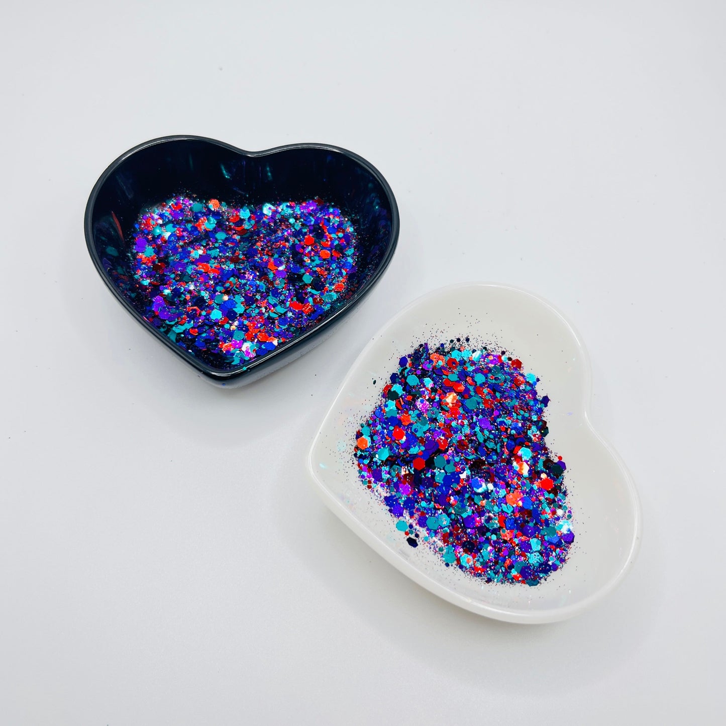 Two heart shaped containers, one black, one white, containing a Teal/Indigo/Red/Purple chunky glitter mix.