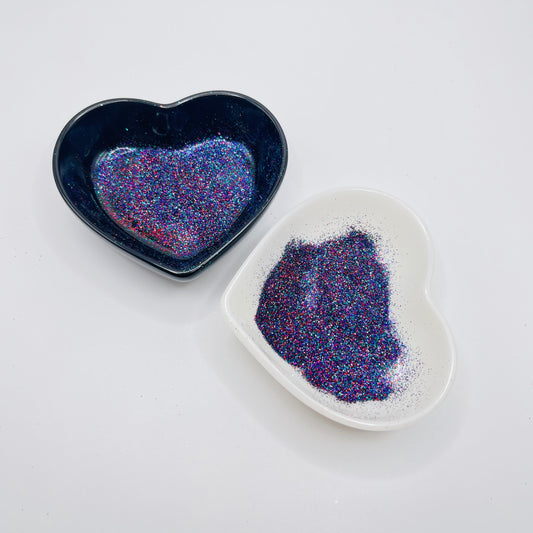 Two heart-shaped dishes, one black and one white, containing multicolored glitter.