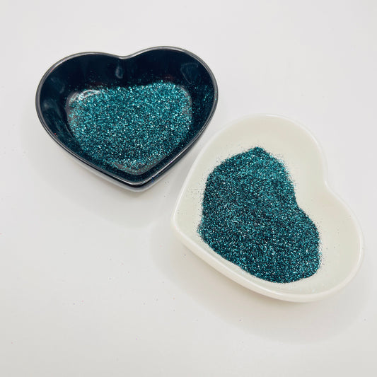 Two heart-shaped dishes, one black and one white, containing multicolored glitter.