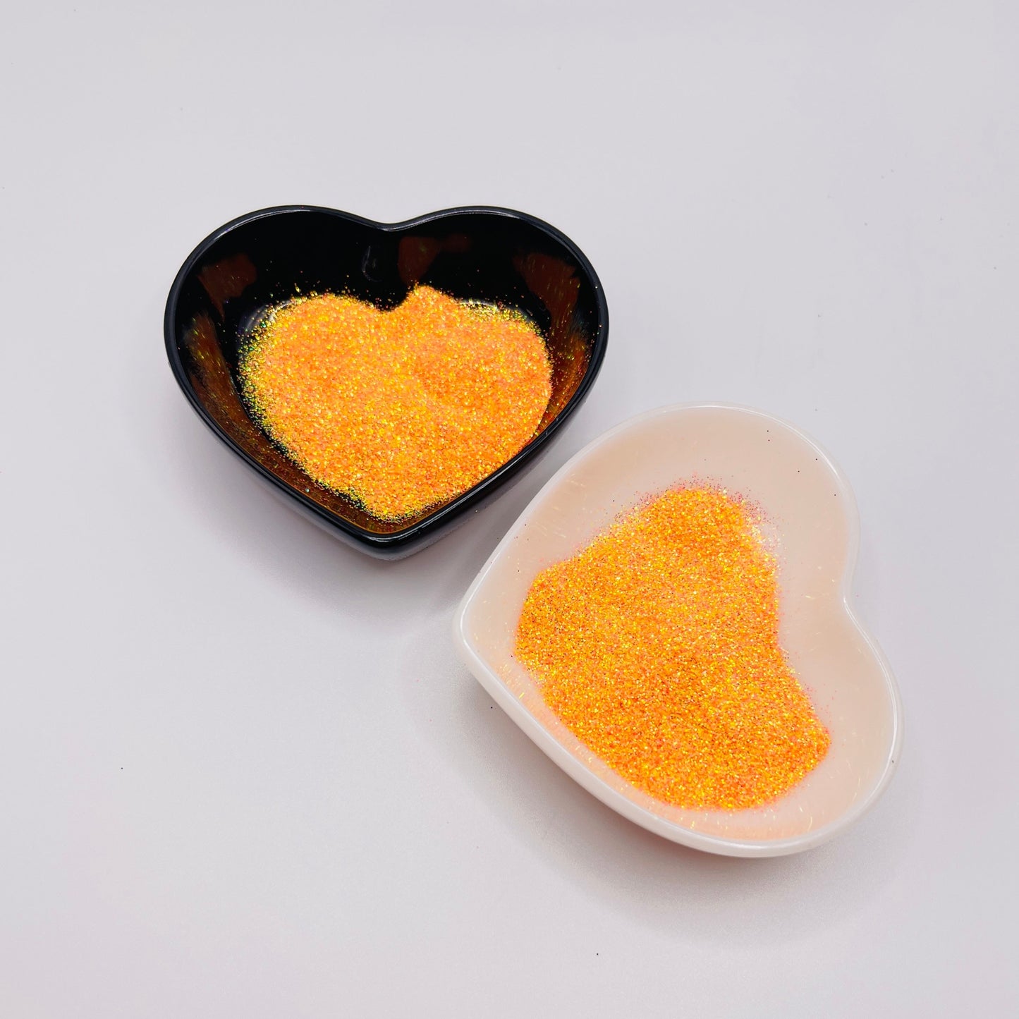 Two heart-shaped dishes containing orange-colored glitter, one black and one white.