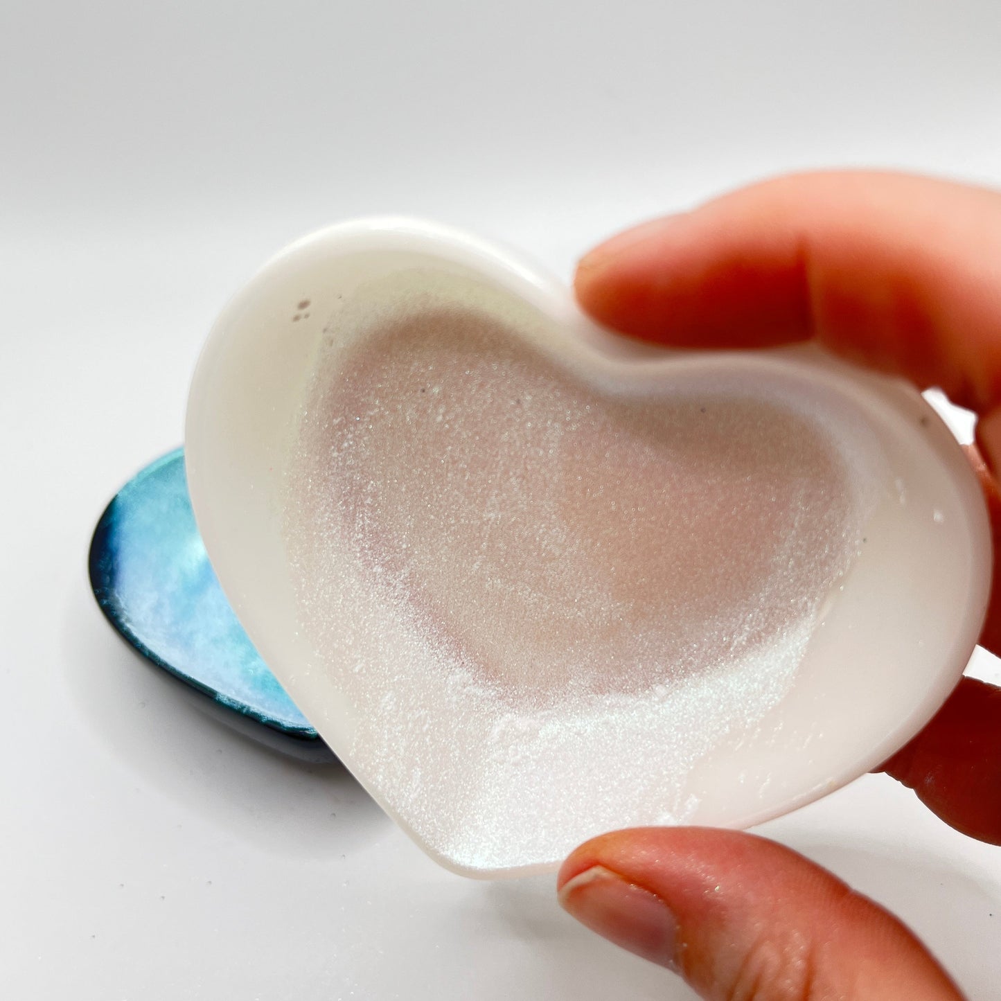 Fingers holding a white heart shaped dish with a white chameleon mica powder.