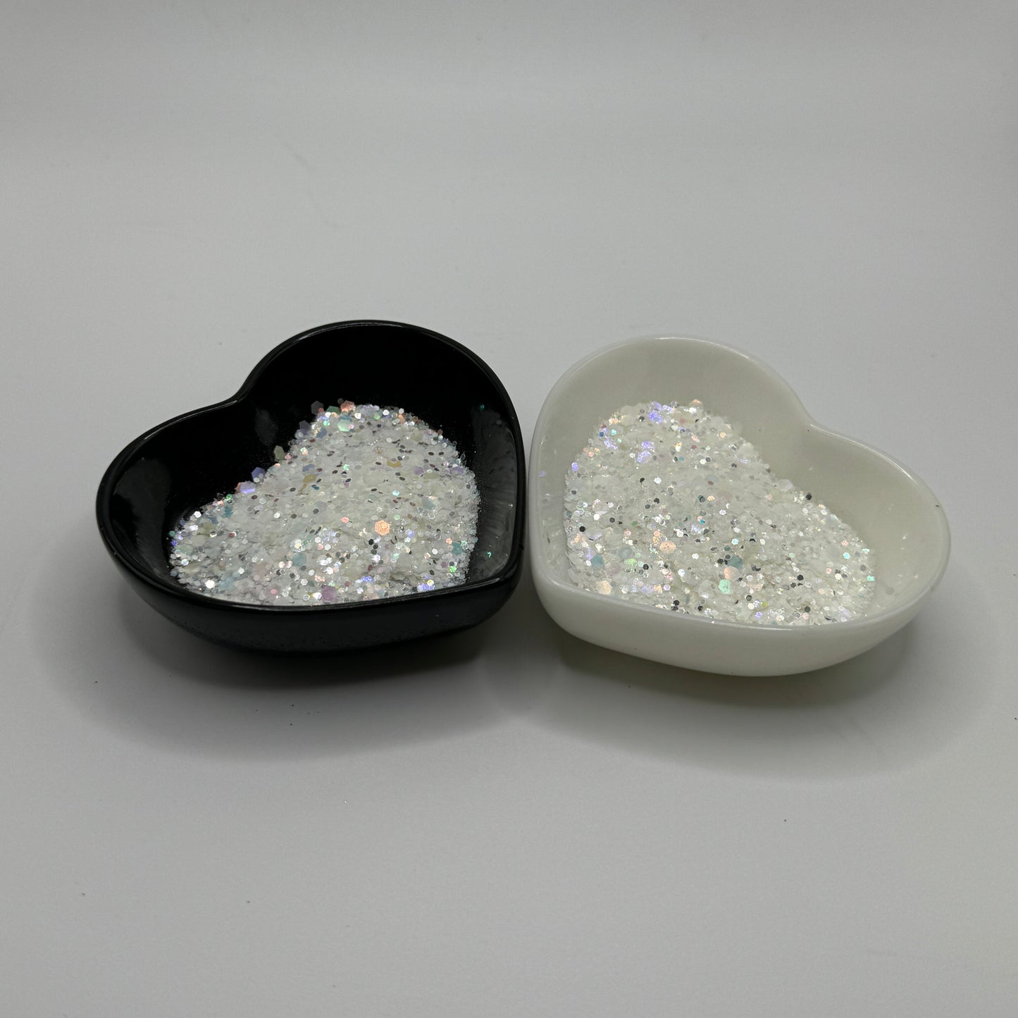 Two heart-shaped containers of glitter, one black and the other white, both showing a chunky white glitter mix
