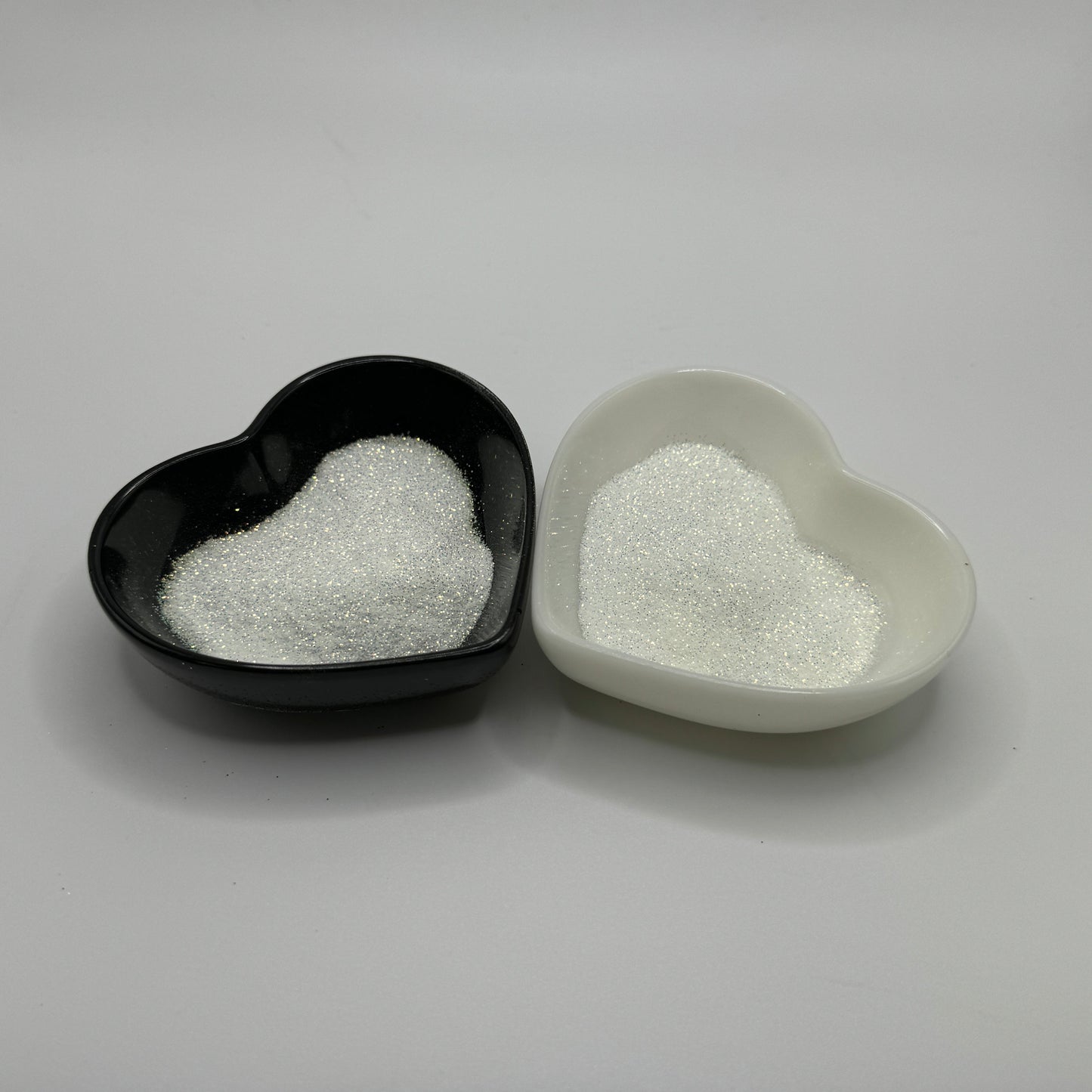 Two heart-shaped containers of glitter, one black and the other white, both showing an extra fine, white glitter
