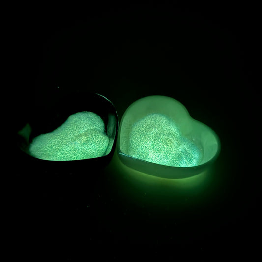 A heart-shaped container filled with glow-in-the-dark glitter, placed on a dark surface.