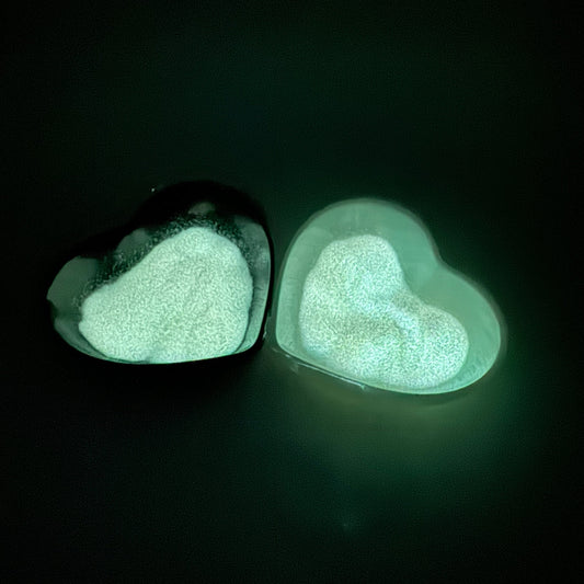 Two heart-shaped containers with glowing glitter inside, placed on a dark surface.
