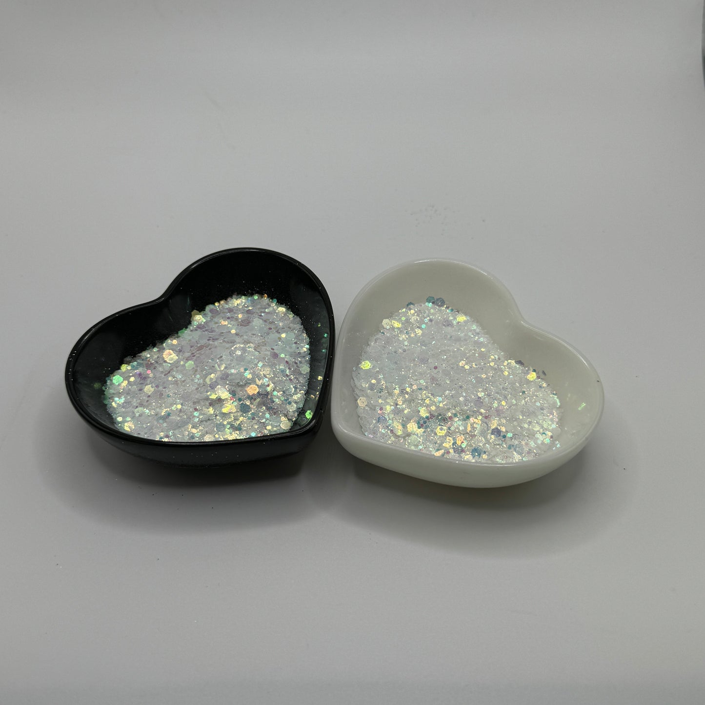 Two heart-shaped containers of glitter, one black and the other white, both showing a chunky, white glitter mix