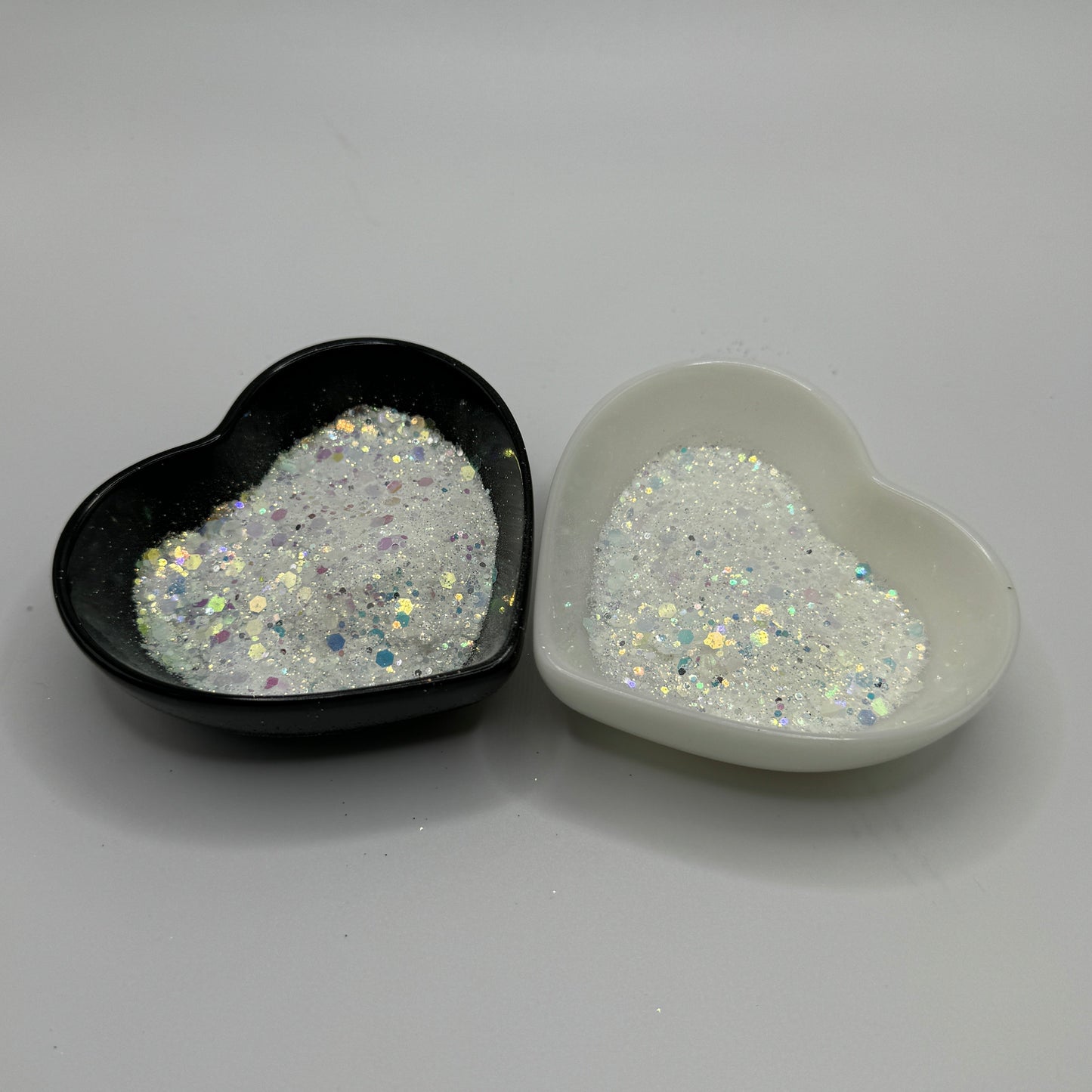 Two heart-shaped containers of glitter, one black and the other white, both showing a chunky white glitter mix