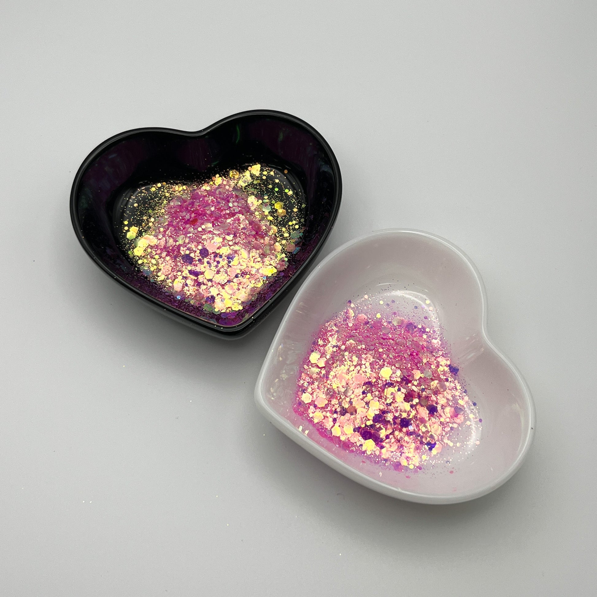 Two heart-shaped dishes, one black and one white, containing light pink chunky glitter mix.