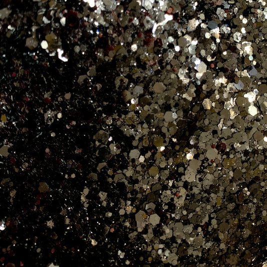 A close-up image of black polyester glitter with various sizes reflecting light, creating a shiny and sparkling appearance.