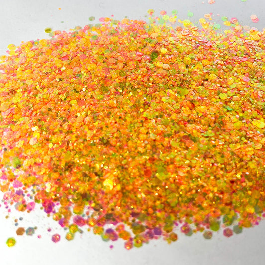 A pile of mixed colours of chunky glitter, including Orange/Pink/Green/Coral on a white background.
