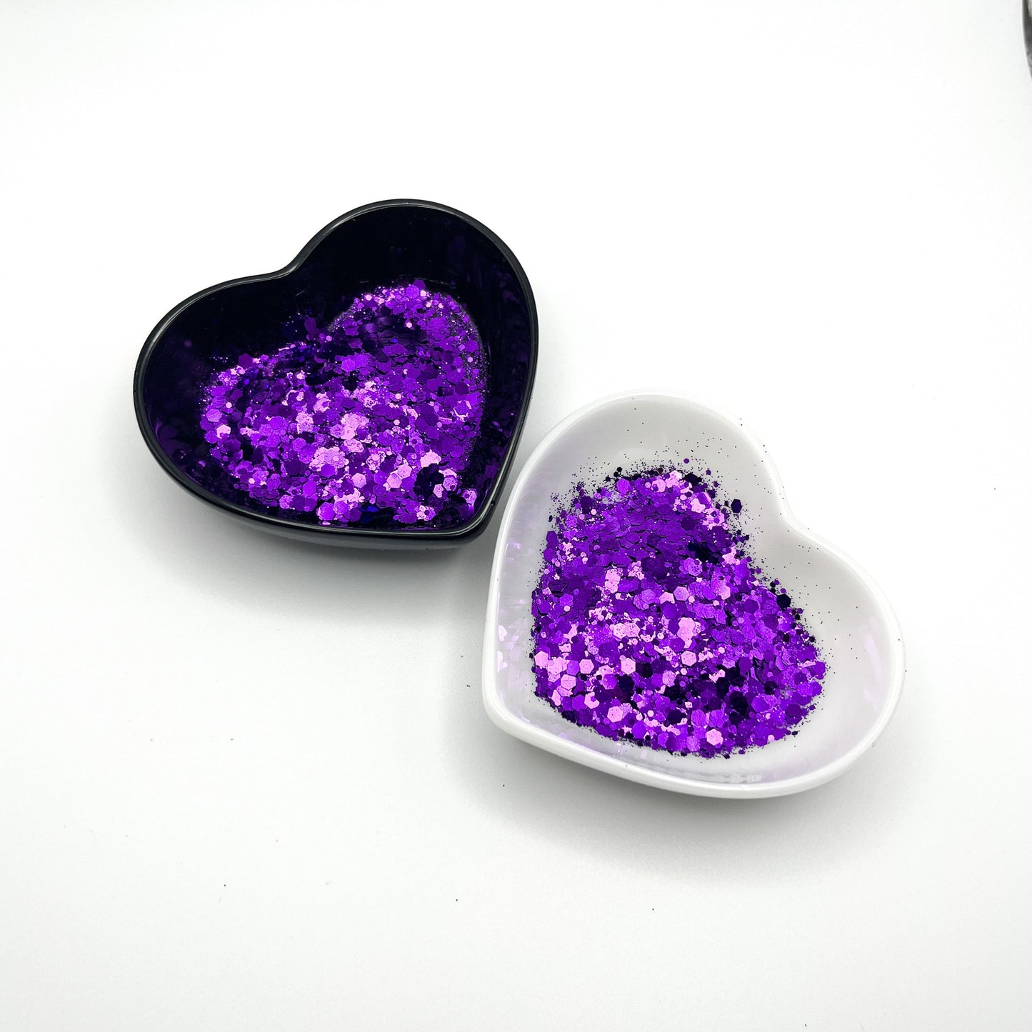 Two heart shaped containers, one black, one white, containing a Purple chunky glitter mix.