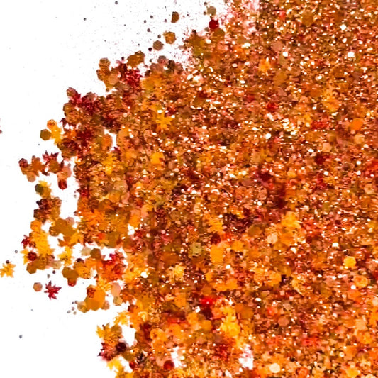 A pile of mixed colours of chunky glitter, including Burgundy/Bronze/Gold/Red/Burnt Orange Hexagons and Leaves on a white background.