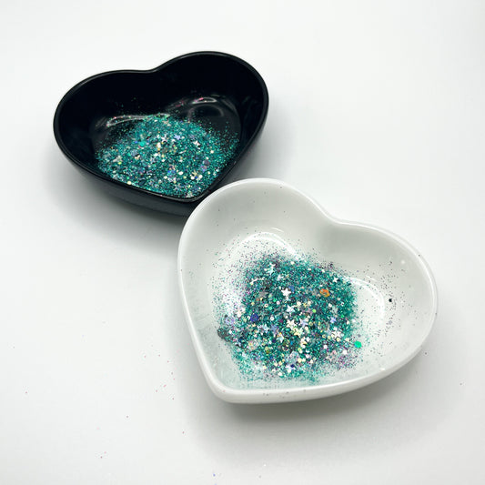 Two heart shaped containers, one black, one white, containing a Teal/Purple/Silver chunky glitter mix with hexagons and stars.