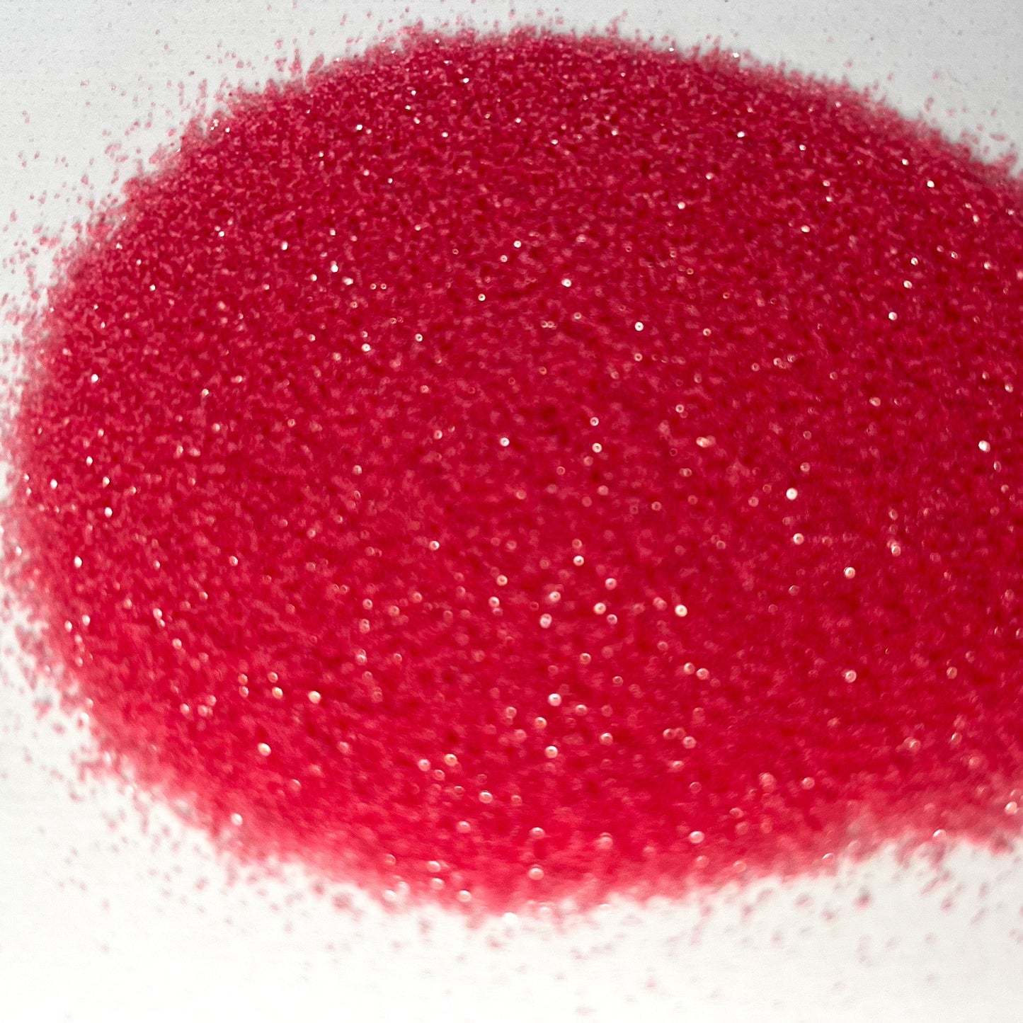 A pile of berry pink, extra fine, iridescent glitter spread on a white surface.