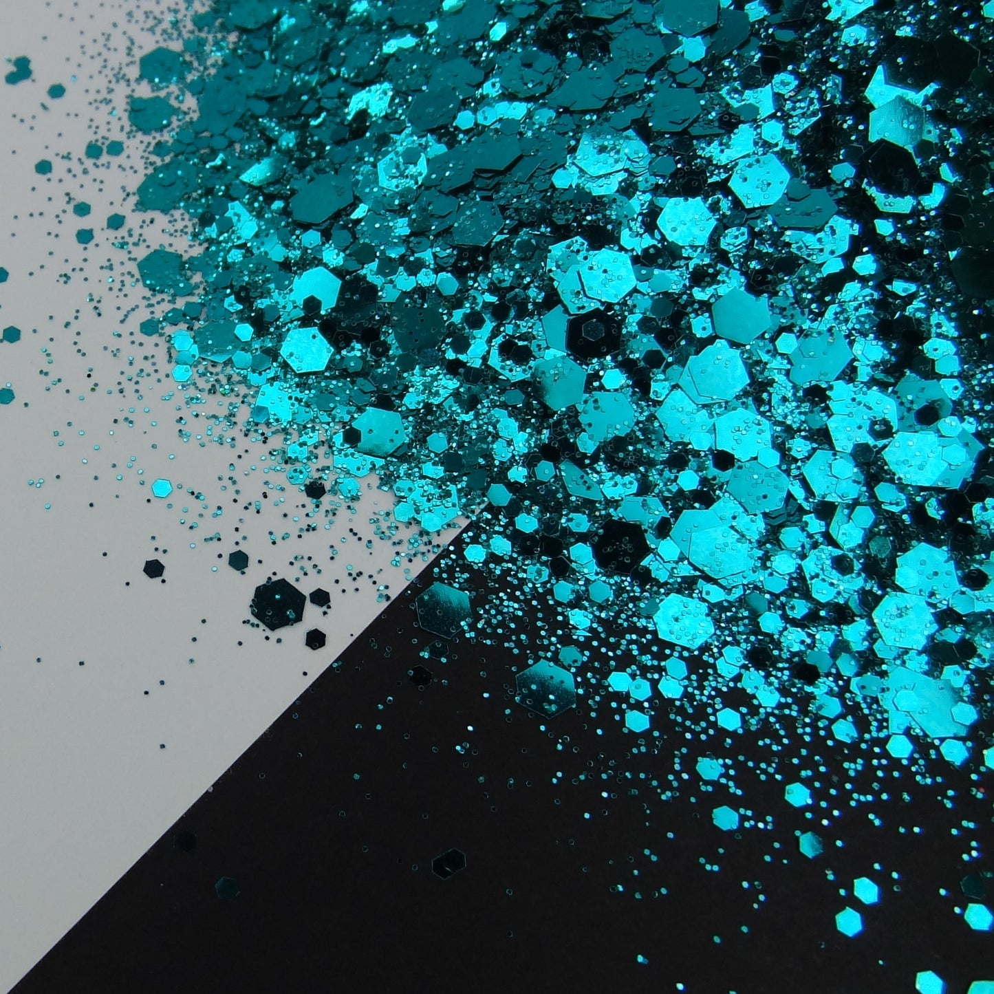 A pile of dark teal chunky glitter on a black and white background.