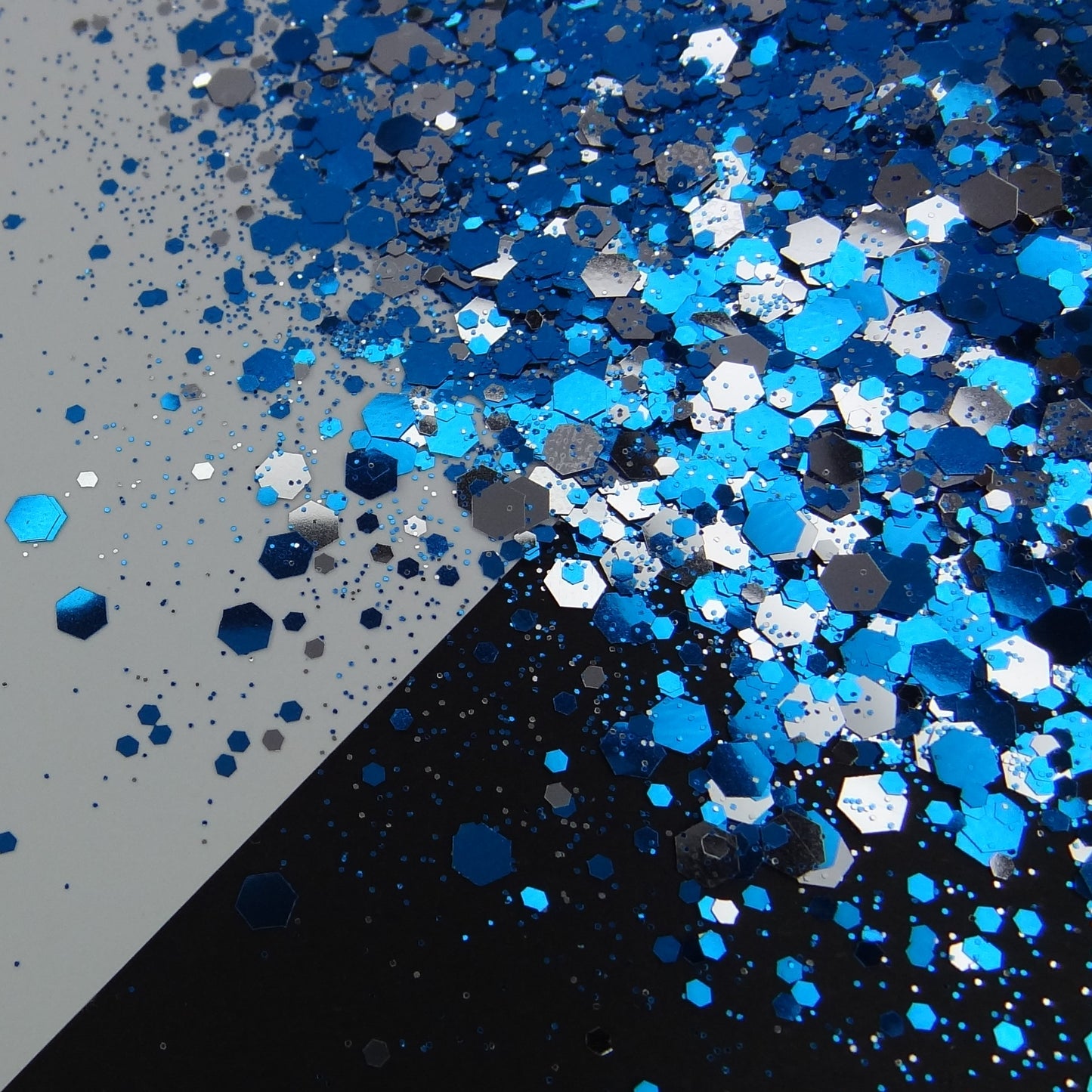 A blue and silver chunky glitter mix spread out on a black and white background.