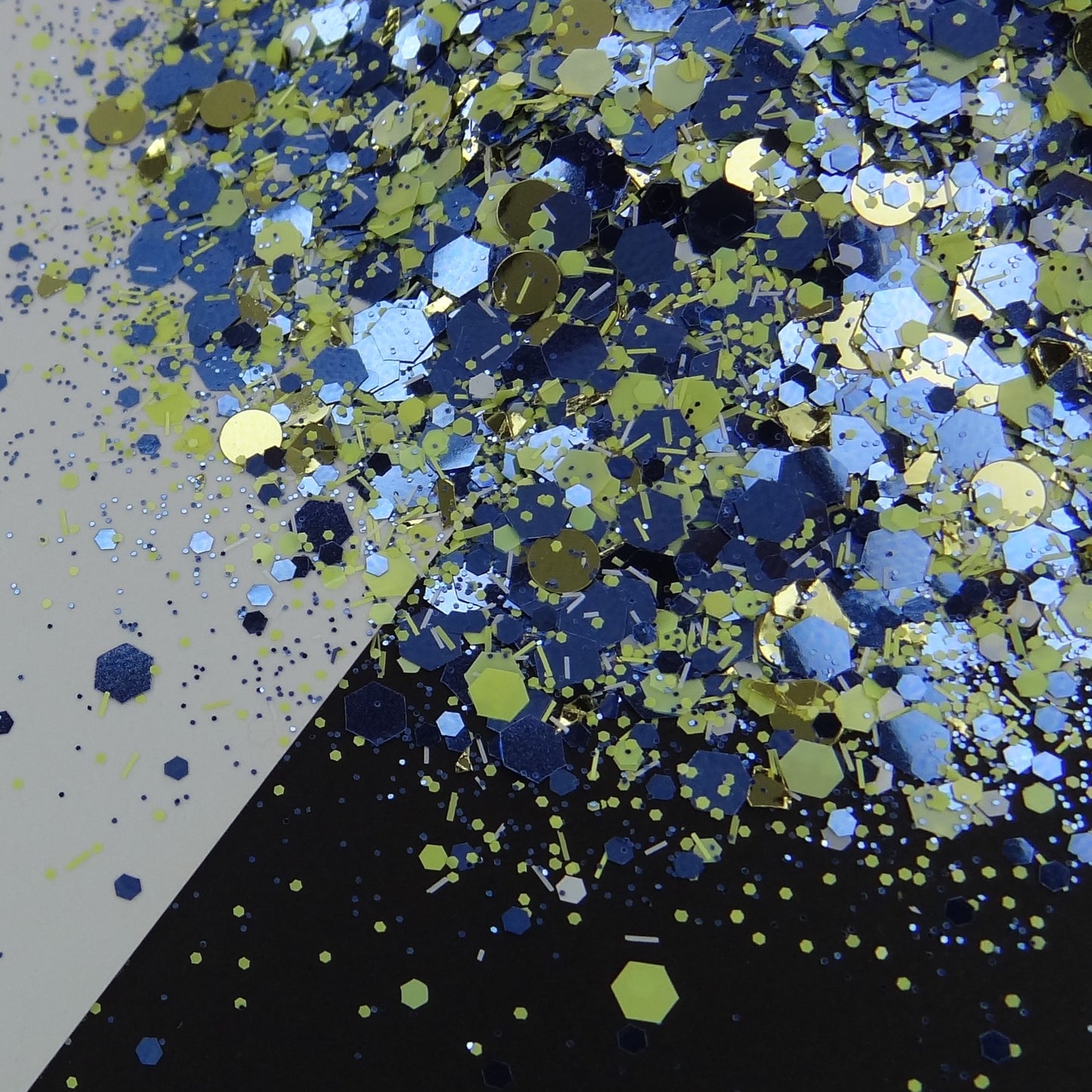 A pile of mixed colours of chunky glitter, including Blue/Yellow/White/Silver on a white and black background.